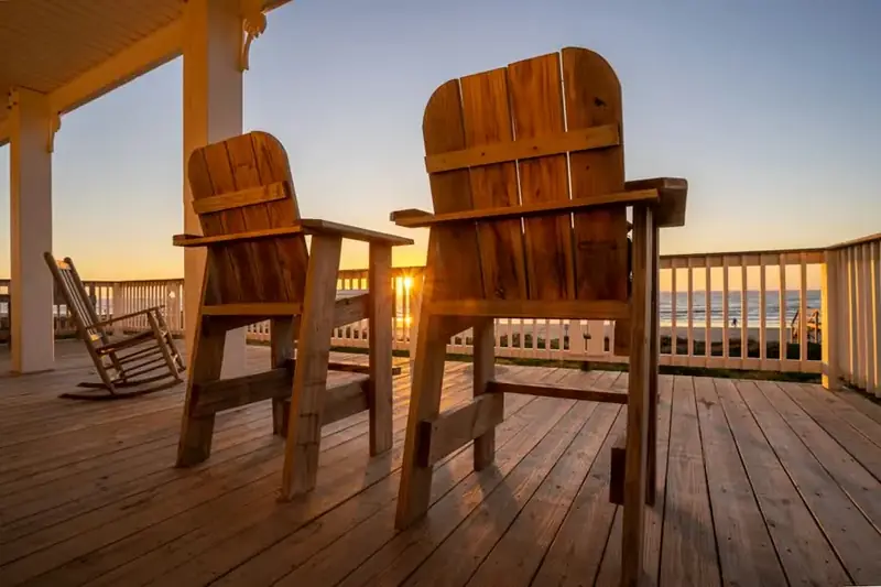 Two wooden chairs facing the sunset on a porch